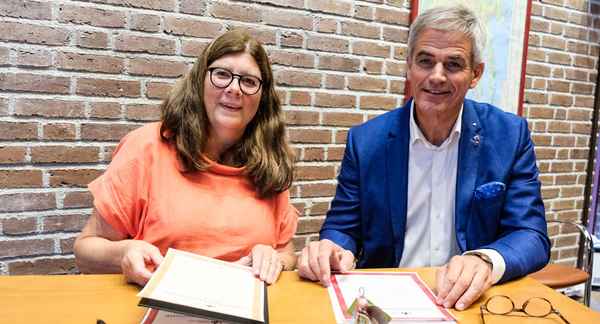 En dame sitter til venstre og en mann til høyre. Mannen skriver under avtalen om at Sandefjord skal fortsette å være et trygt lokalsamfunn. Foto.